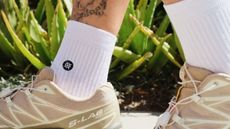 The tattooed ankles of a person wearing a pair of Stance socks and S-Lab trainers