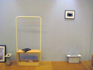 Wooden stand photographed on a wooden floor against a blue wall with a black and white frame hanging