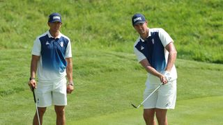 Victor Perez takes a shot during a practice round before the Olympics as his caddie watches