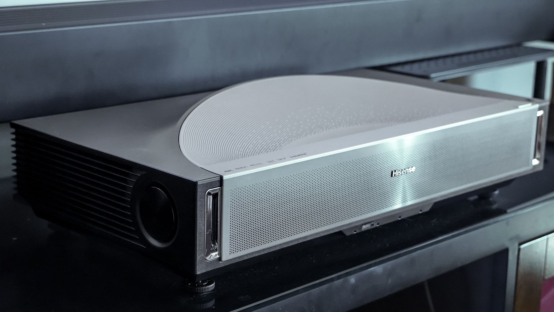 A Hisense PX4 Pro projector on a home media center shelf