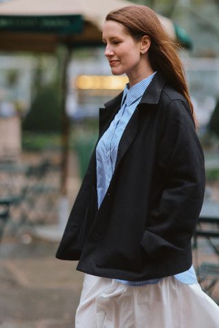 fashion editor Halie LeSavage wears a blue button down shirt with a white skirt and a black jacket