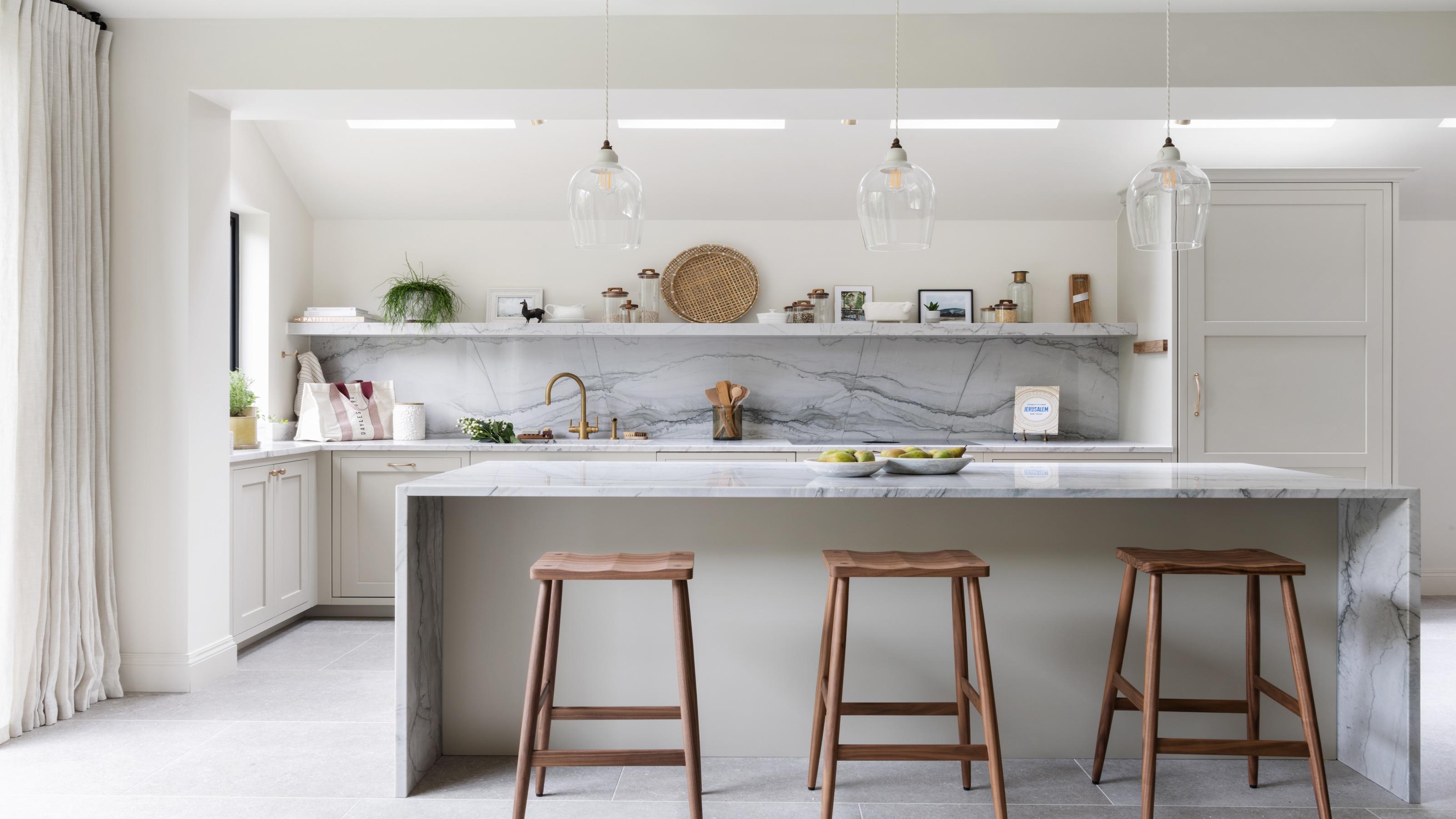 A marble kitchen island with bar stools beside it. There is also a view of the kitchens backsplash and open shelving. 