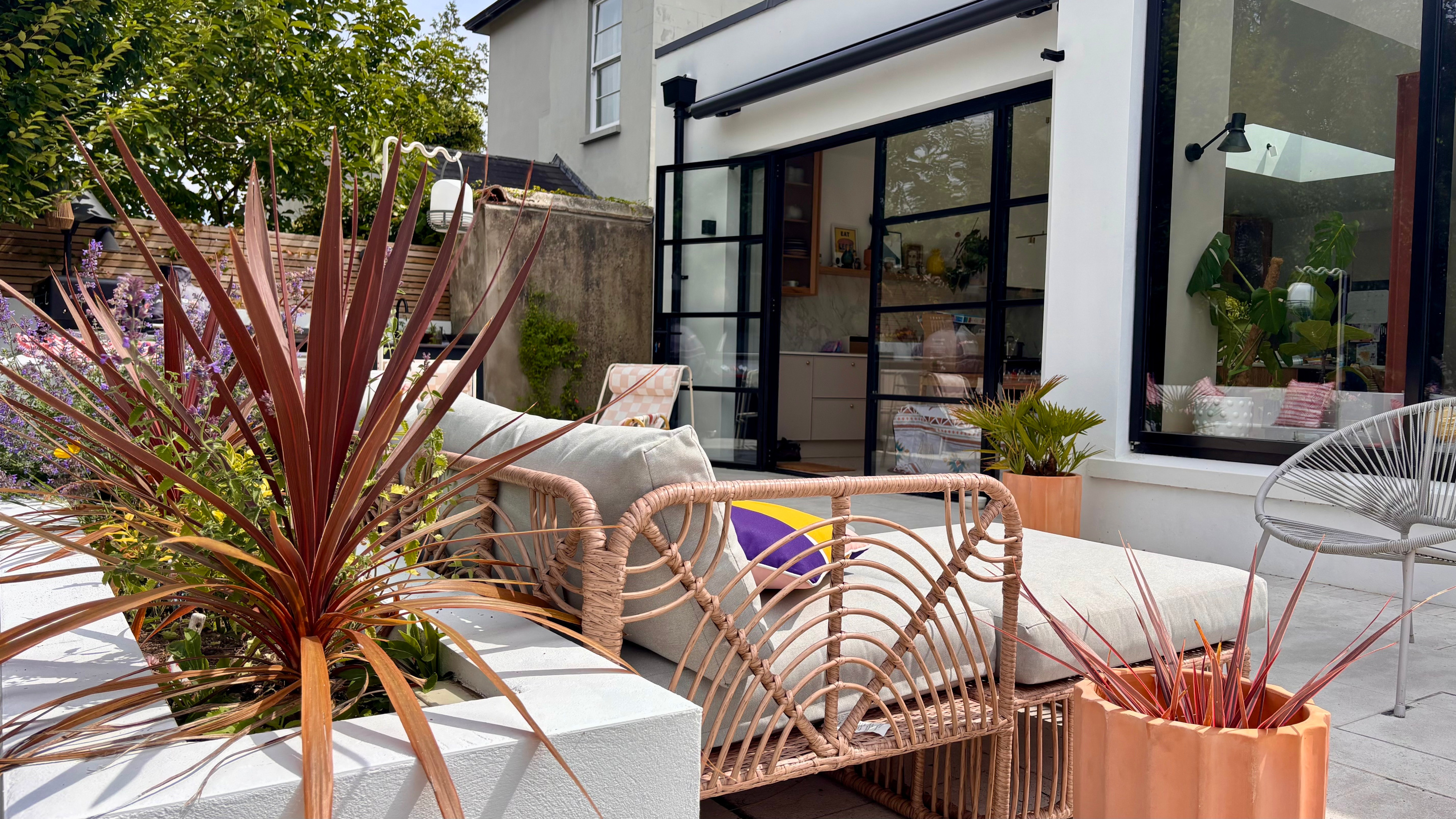 patio with open doors, planting, a crank awning and a grey outdoor sofa