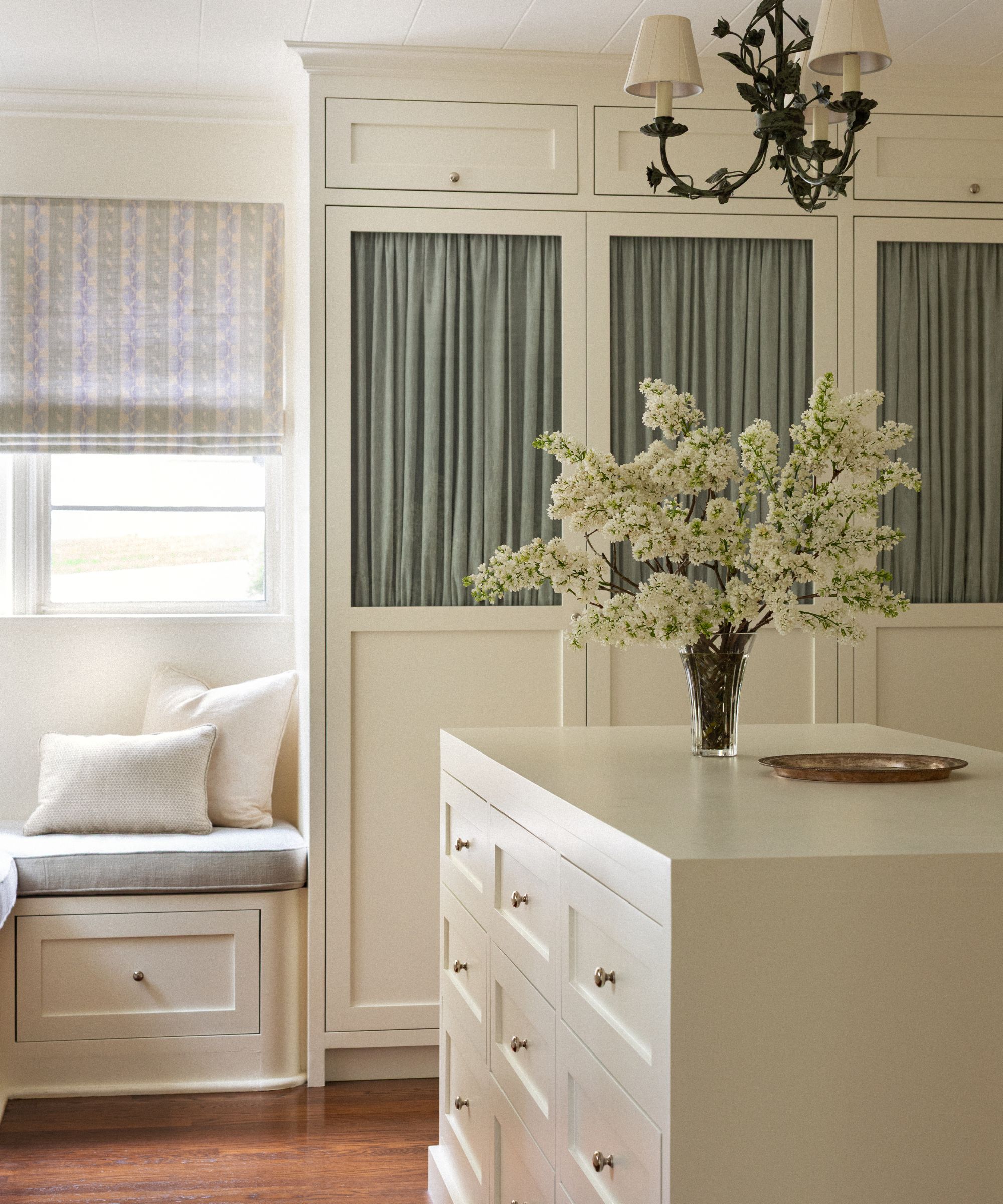 a neutral dressing room with built-in closets with green fabric curtains in the cabinetry, a center island and banquette seat