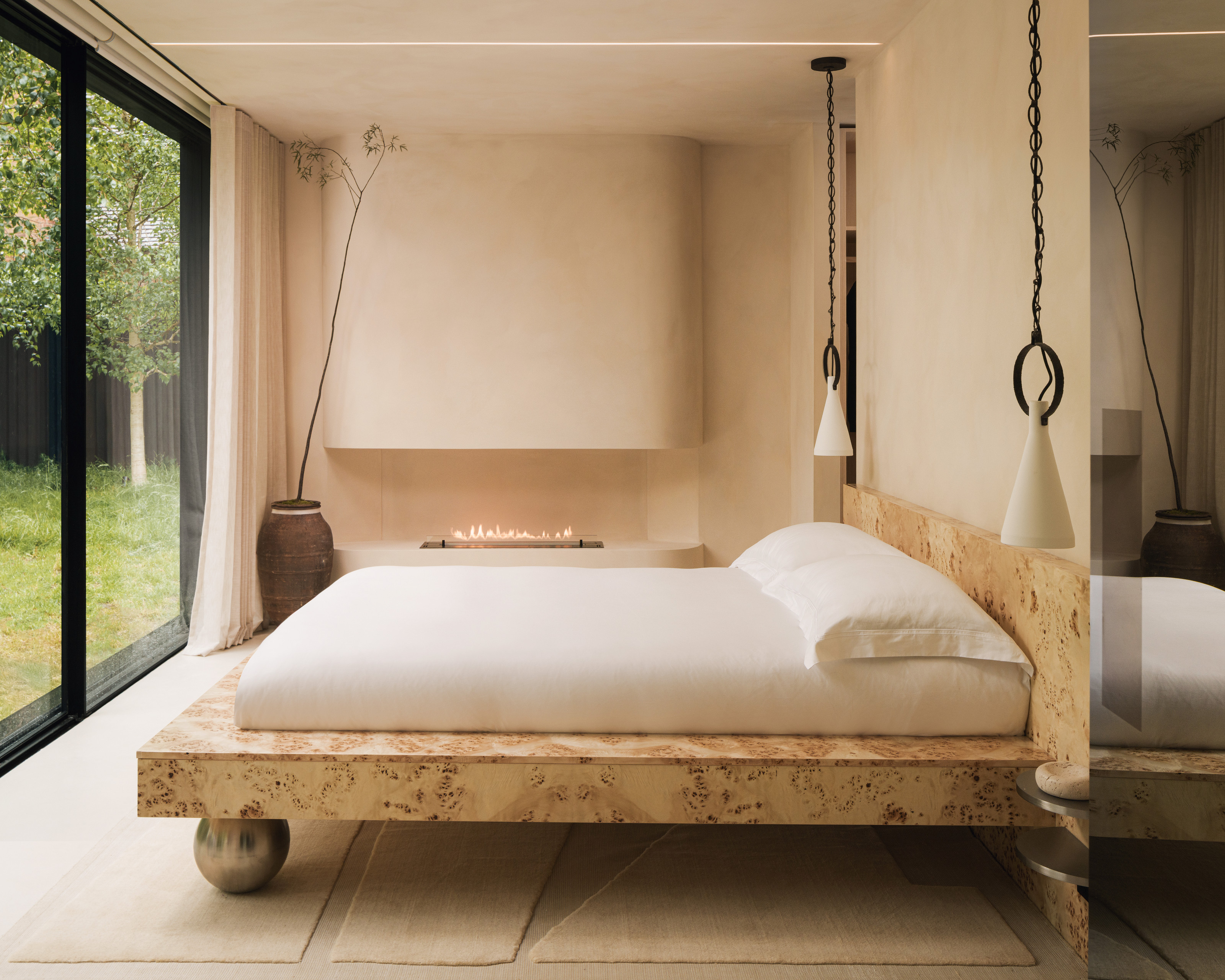 Bedroom with burl wood bed with rounded foot, plaster fireplace, pendants either side of the bed and cream cut-out carpet