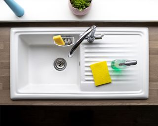 A directly above shot of a clean kitchen sink, a sponge and washing up liquid can be seen near by