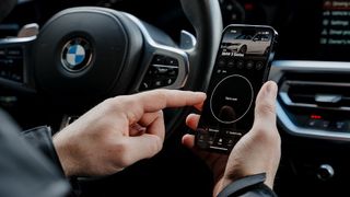 A pair of outstretched hands holding smartphone with the OBDeleven app open on screen behind the wheel of a BMW