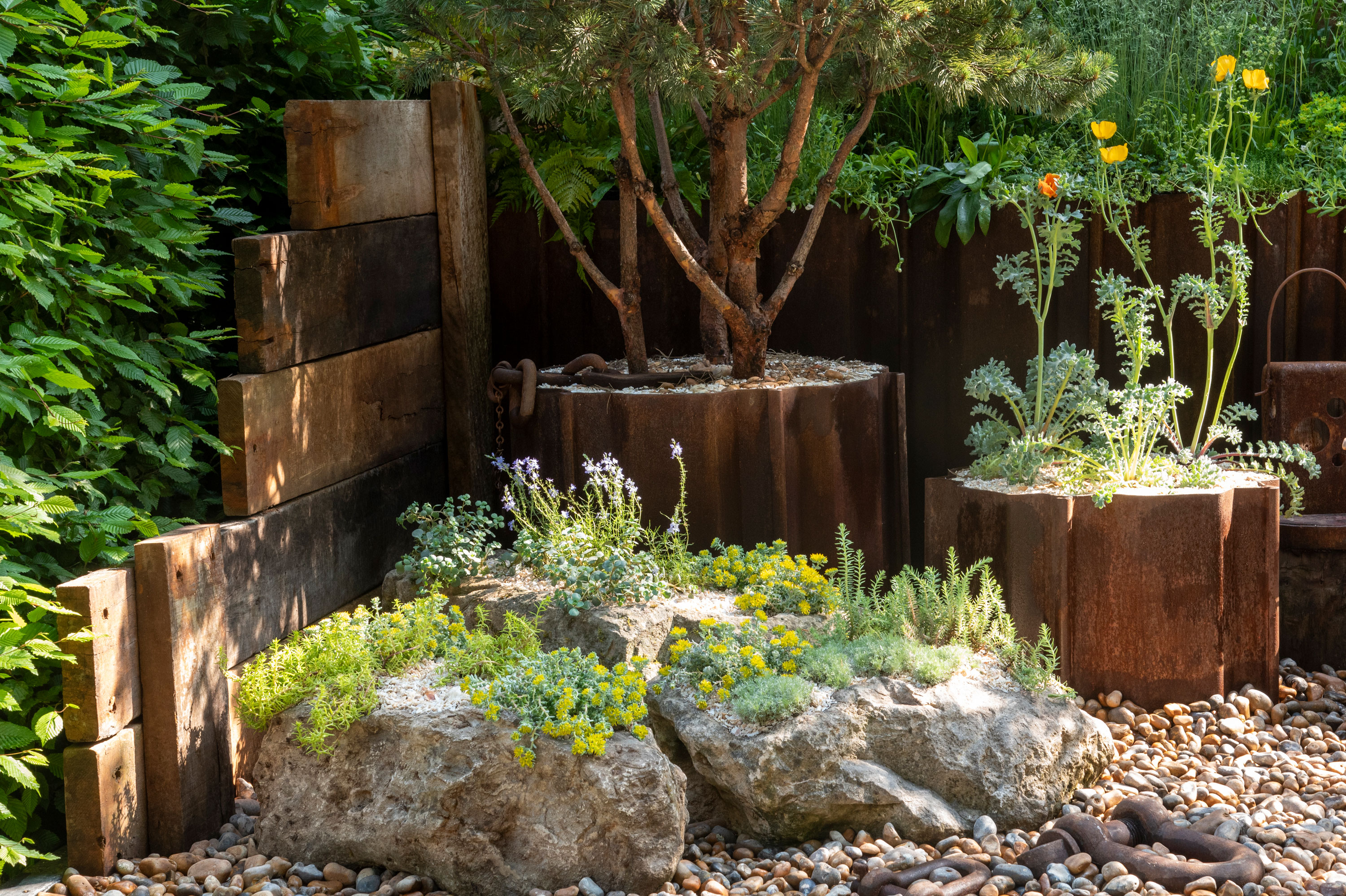 rock garden with boulders and gravel, with succulent planting and containers filled with trees and flowers