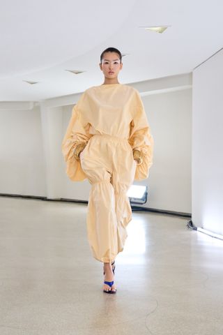 seorang model mengenakan jumpsuit kuning muda di landasan pacu di Alaïa