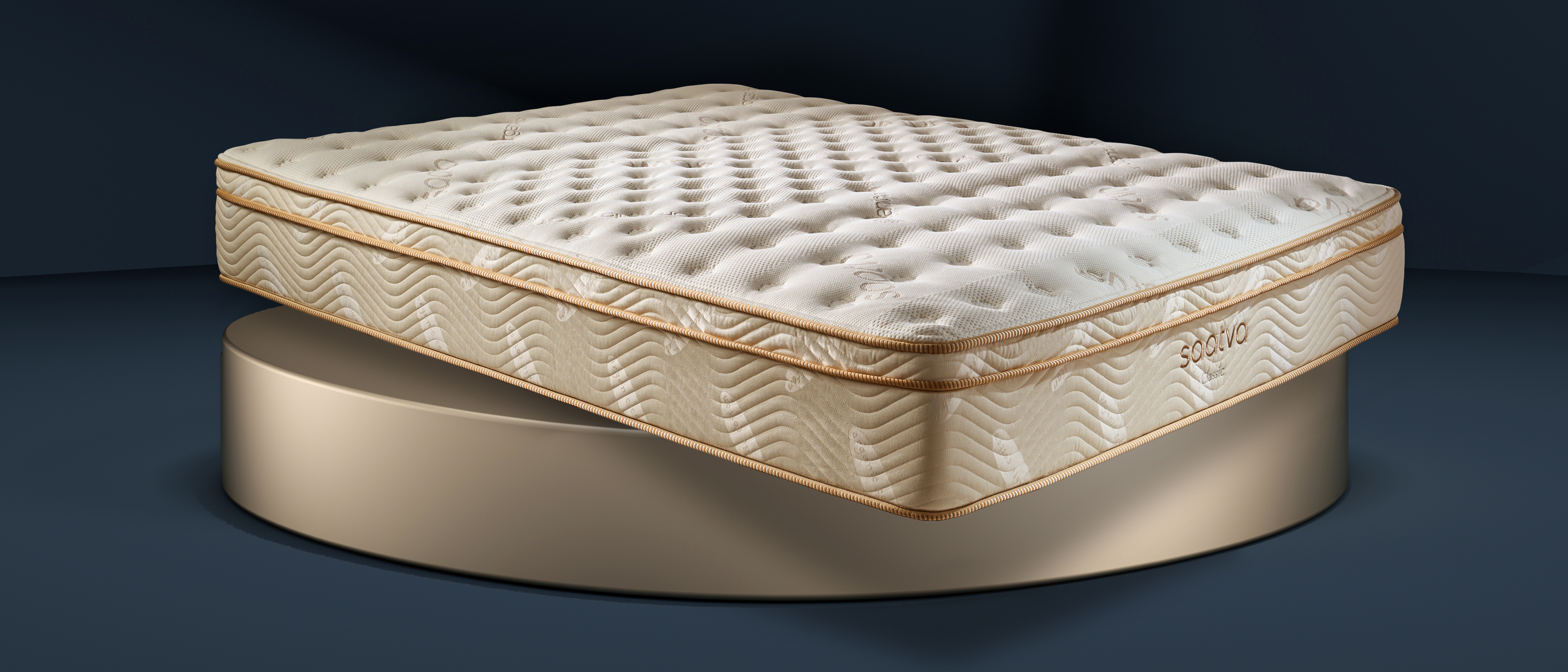 The Saatva Classic mattress photographed in our Sleep Lab during the review process, with the image showing it displayed against a blue-black background and placed on a large round gold plinth to match the golden piping along the edges of the mattress