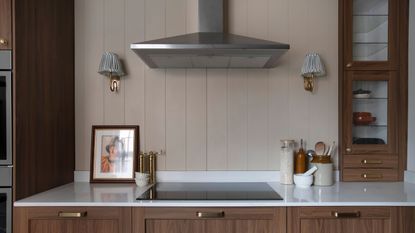 A section of a modern kitchen with wood panelling as the backsplash and a view of the extractor fan as well as the stovetop, cabinet and two wall lights hanging on either side
