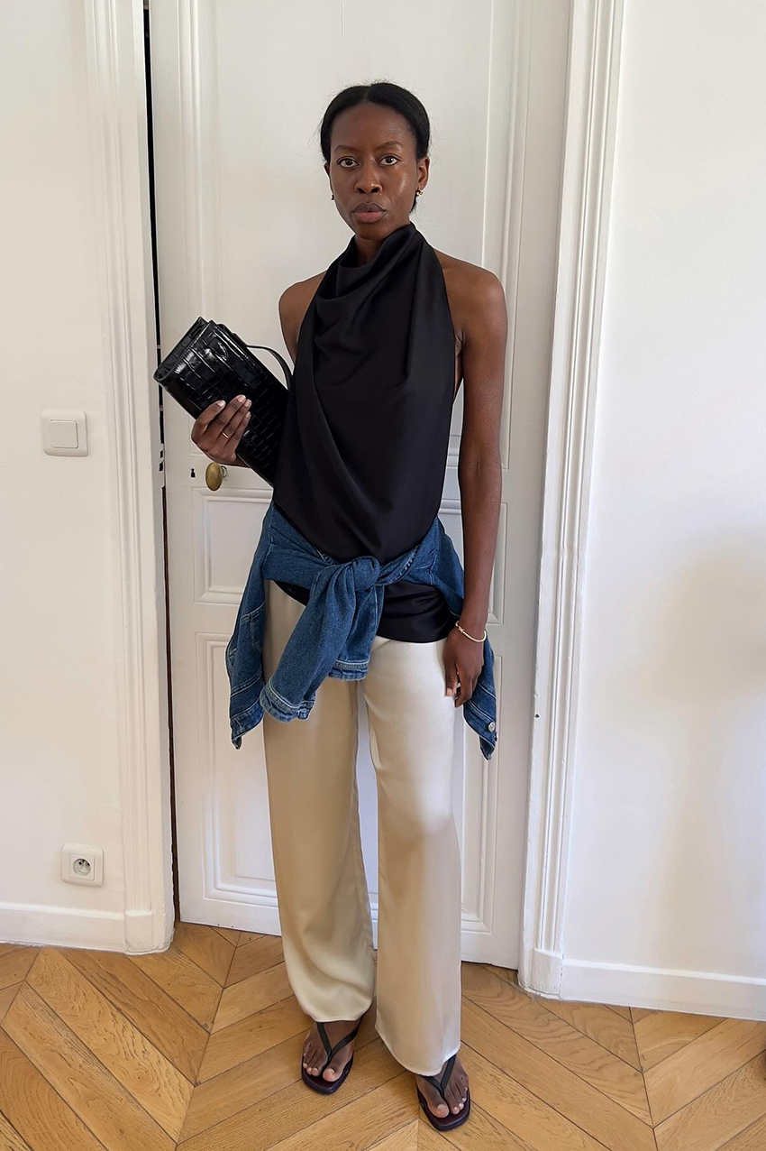 a woman wearing a black cowl neck top and white pants