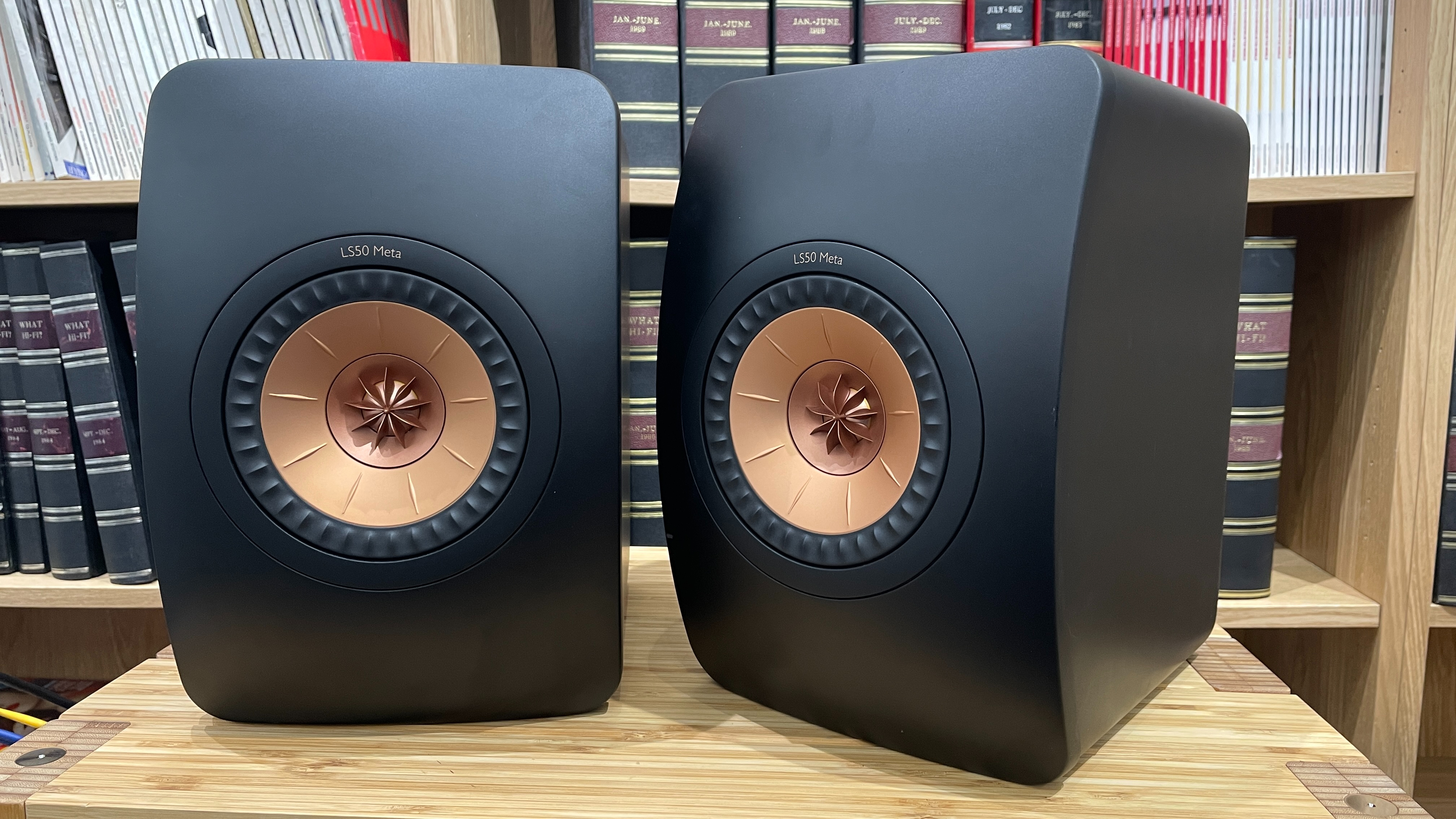 KEF LS50 Meta stereo speakers on wooden equipment rank with books in background