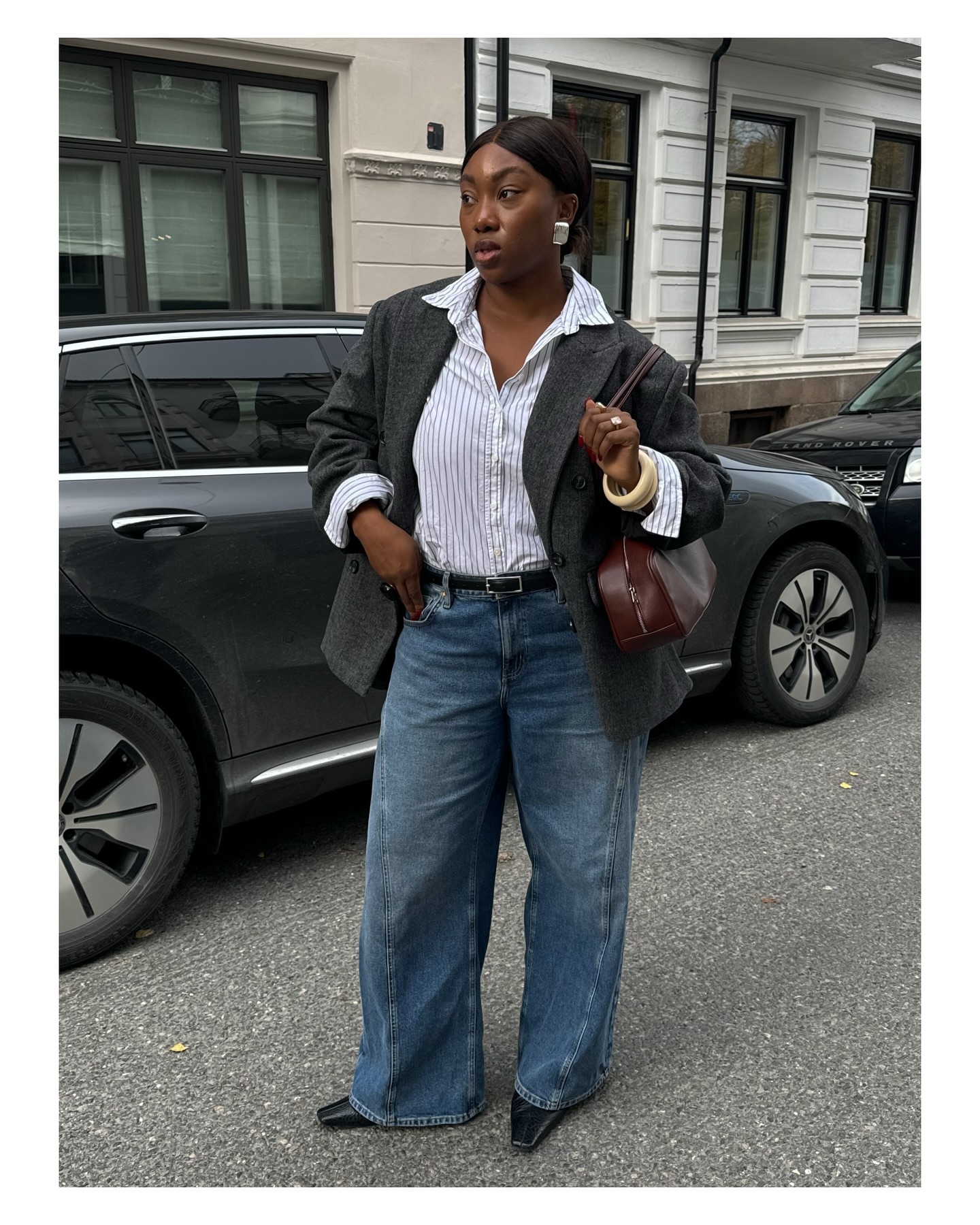 Woman wearing a gray blazer, a white striped button-down, wide-leg jeans, and point-toe shoes.