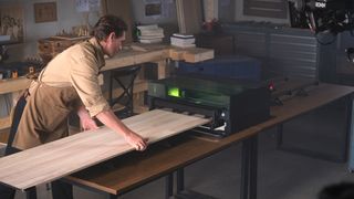 xTool S1; a person pushing a piece of wood through a laser cutter