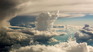 Aerial view of cloudscape against sky. White fluffy clouds will the sky and a flattened sheet of white cloud lies above.