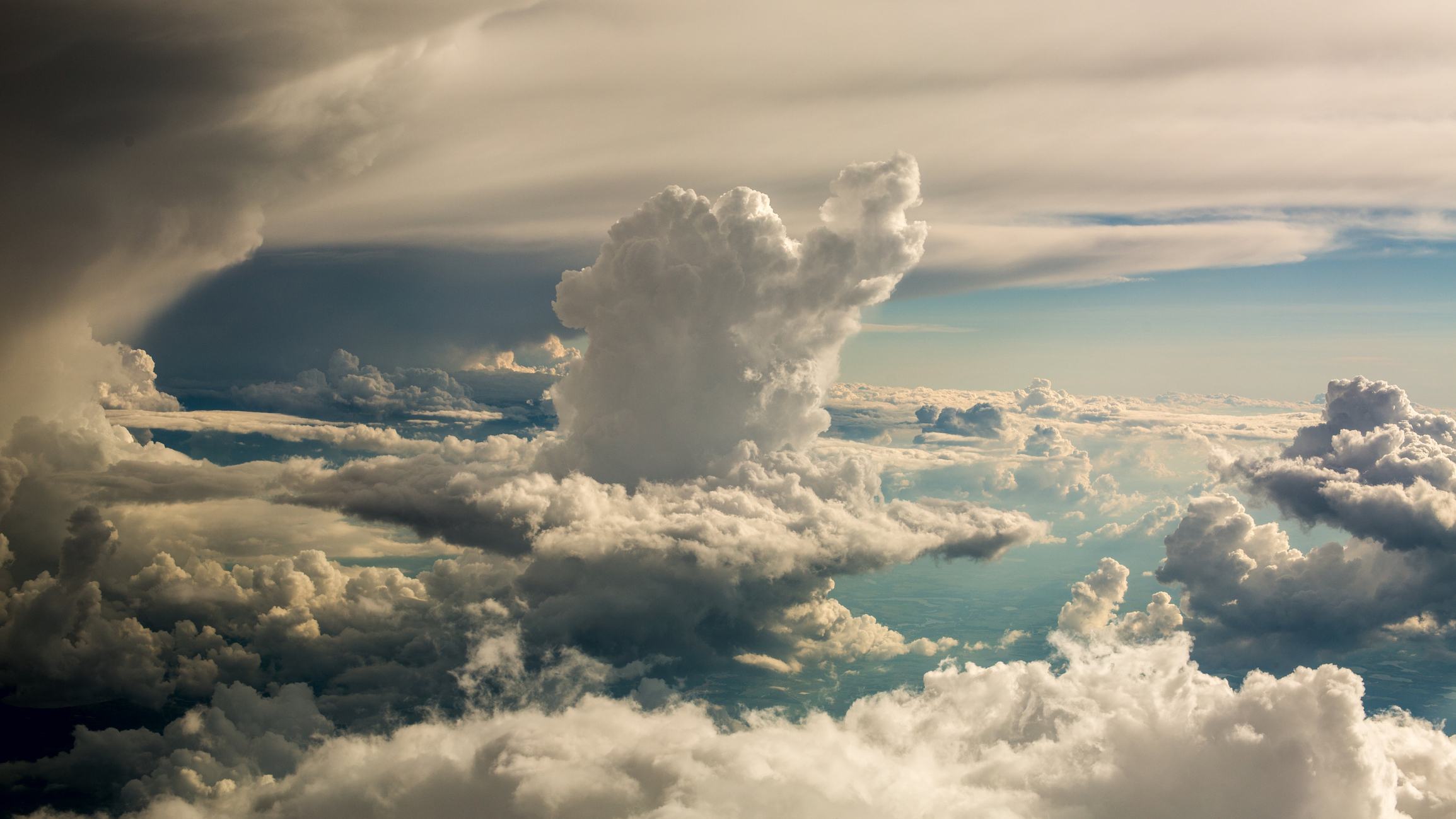 Aerial view of cloudscape against sky. White fluffy clouds will the sky and a flattened sheet of white cloud lies above.
