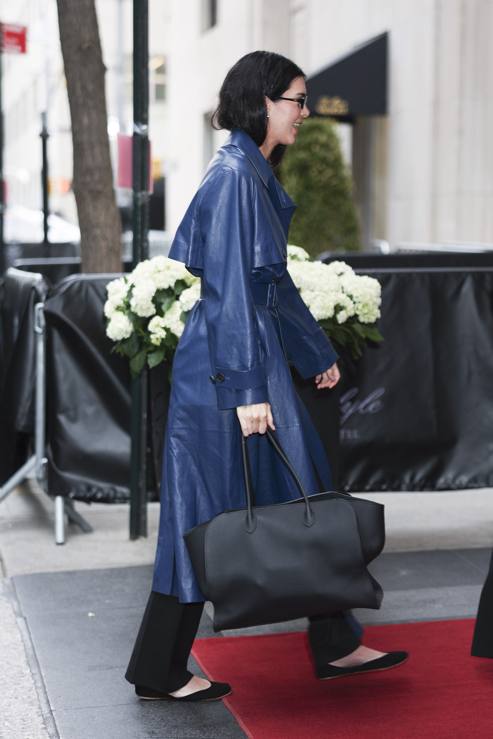 Kendall Jenner wears blue trench coat, black trousers, black ballet flats, carries The Row Marlo bag