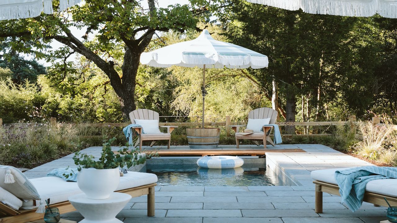 Stylish plunge pool surrounded by wooden chairs, sunbeds, white parasol and trees