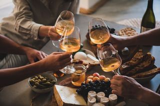 A group of women cheersing wine glasses over a charcuterie board. 