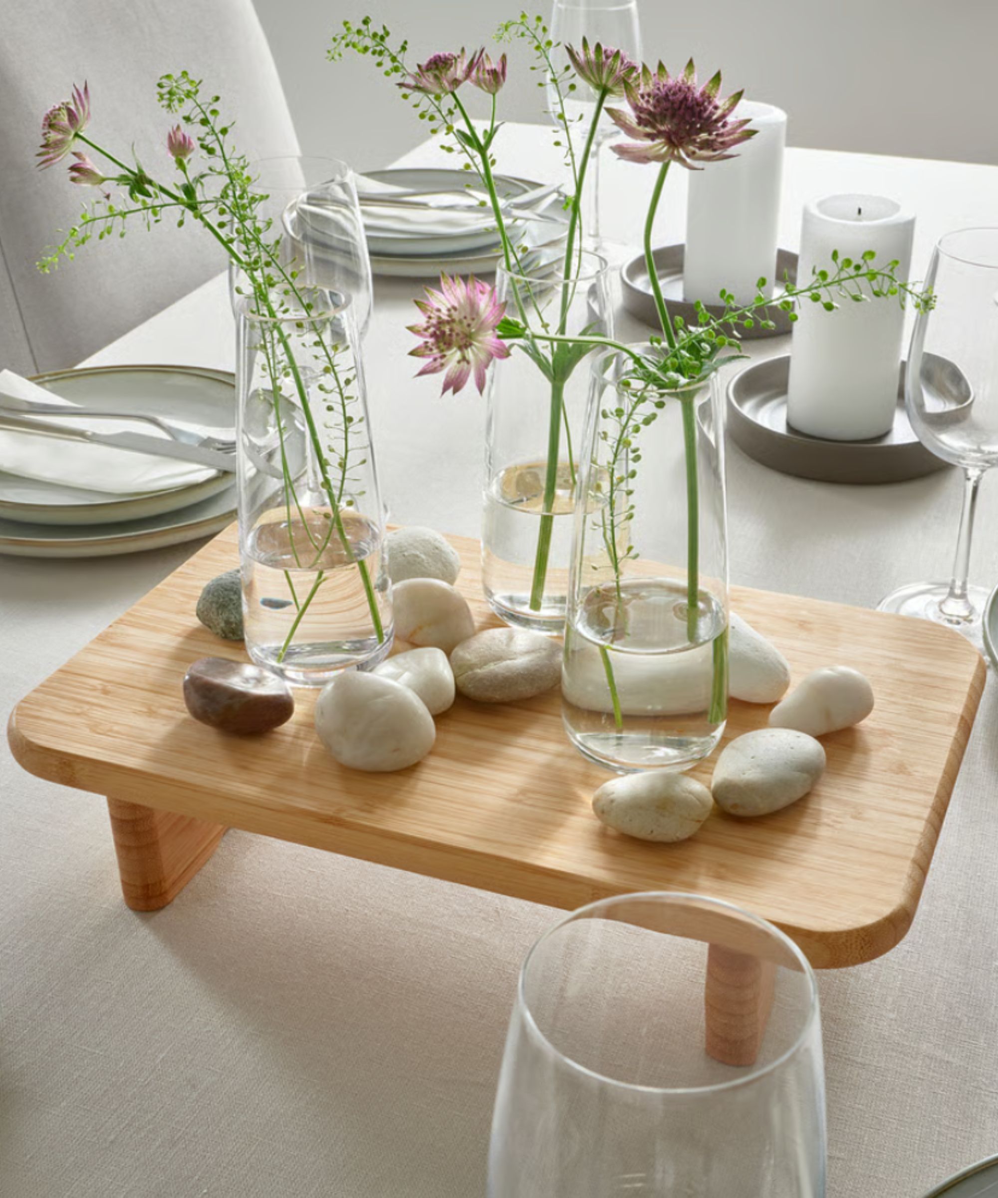 Raised bamboo board with vases of flowers and pebbles on in the center of the table
