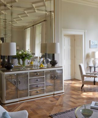 mirror accent wall in a traditional neutral dining room with a mirrored stainless steel console styled with a pair of lamps