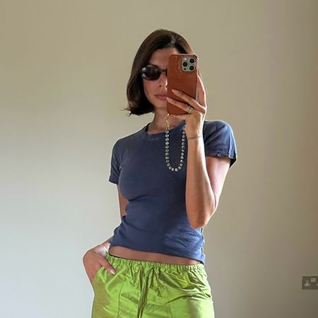 a woman wearing a blue t-shirt, green taffeta pants, and beaded sandals