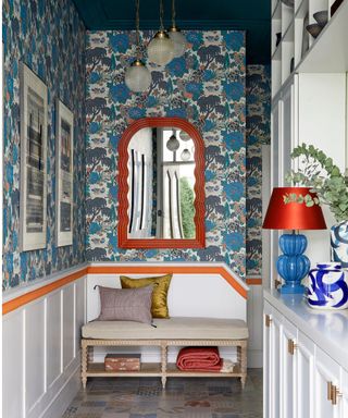 entryway with bold blue wallpaper and orange mirror and wall stripe