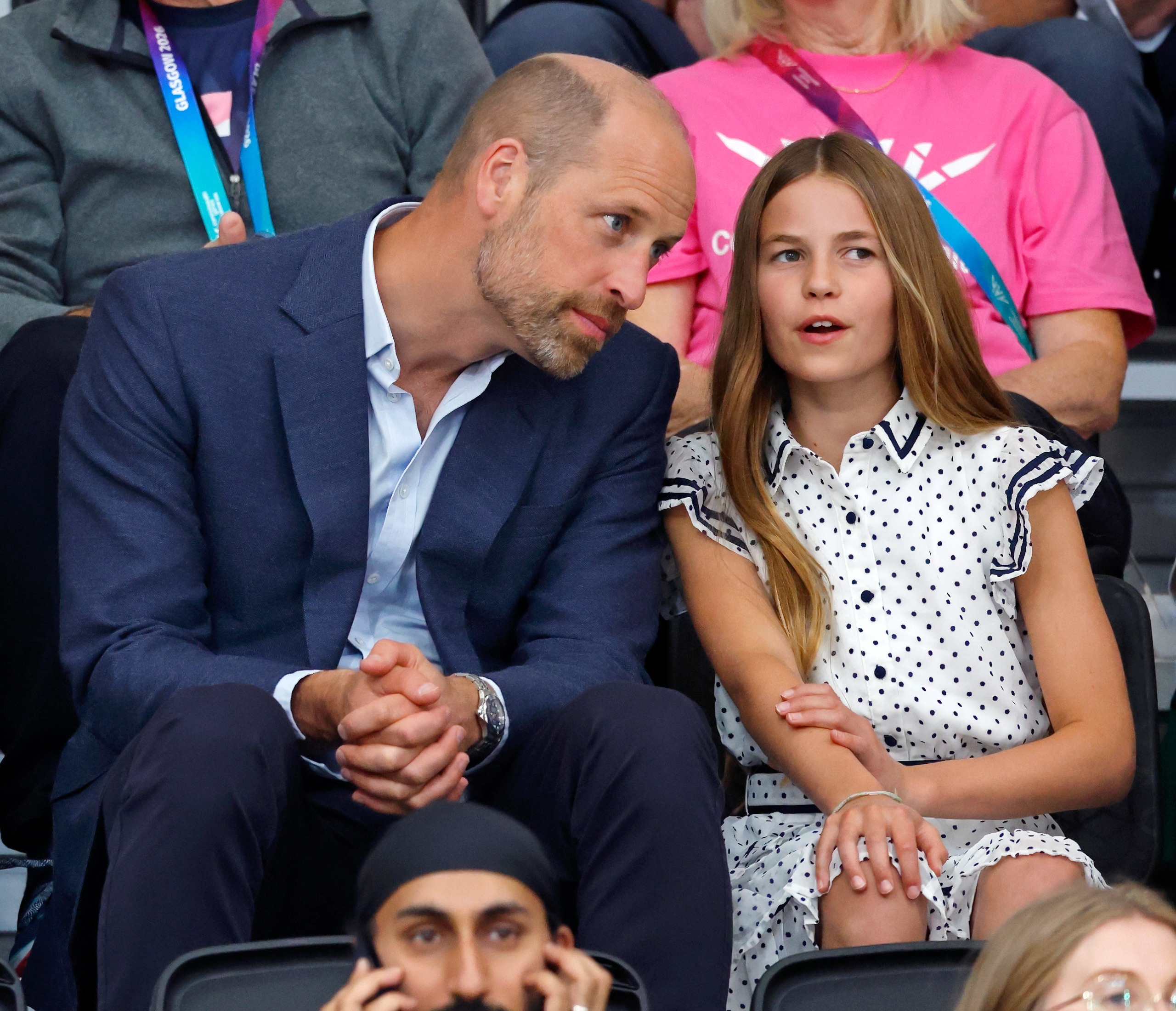 Prince William wearing a blue suit sitting and talking to Princess Charlotte