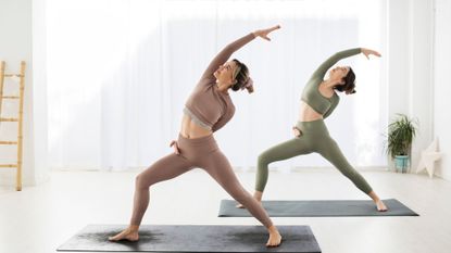 Two women practice yoga side by side after downloading one of the best yoga apps