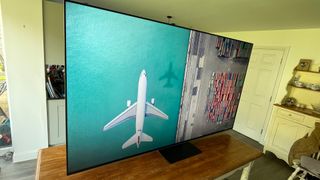 TCL 85C805K 4K TV slight angle on dining table showing aircraft on screen