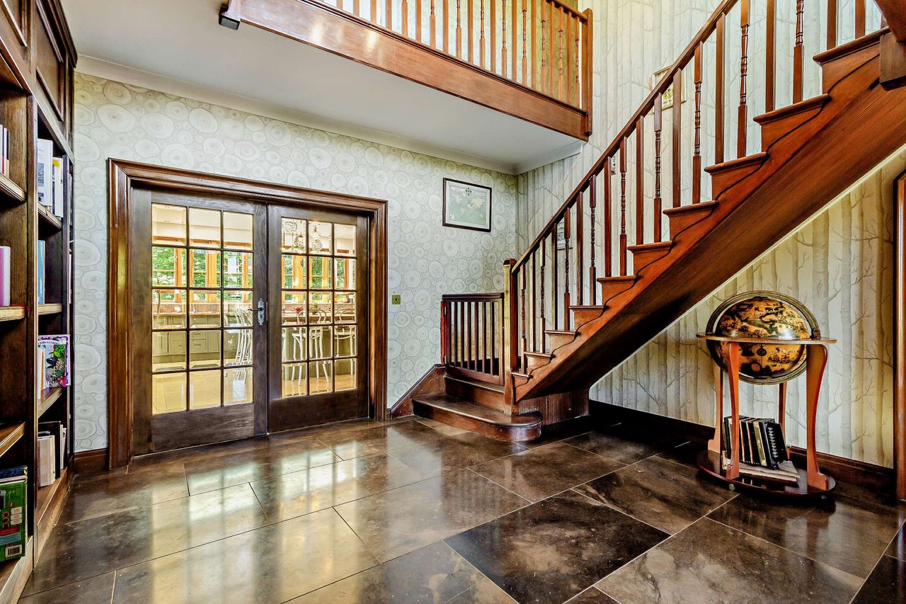A wooden staircase with black marble flooring beneath sitting opposite a bookcase and leading to the kitchen-dining room