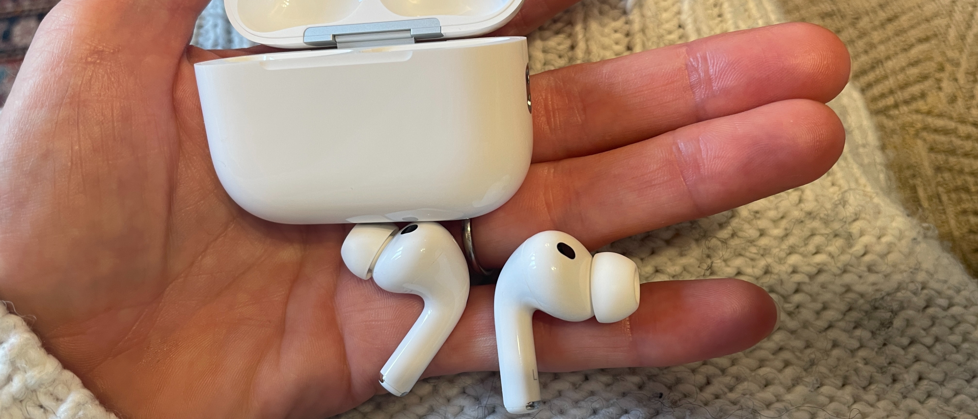 AirPods Pro 3 held in hand on a woollen beige background