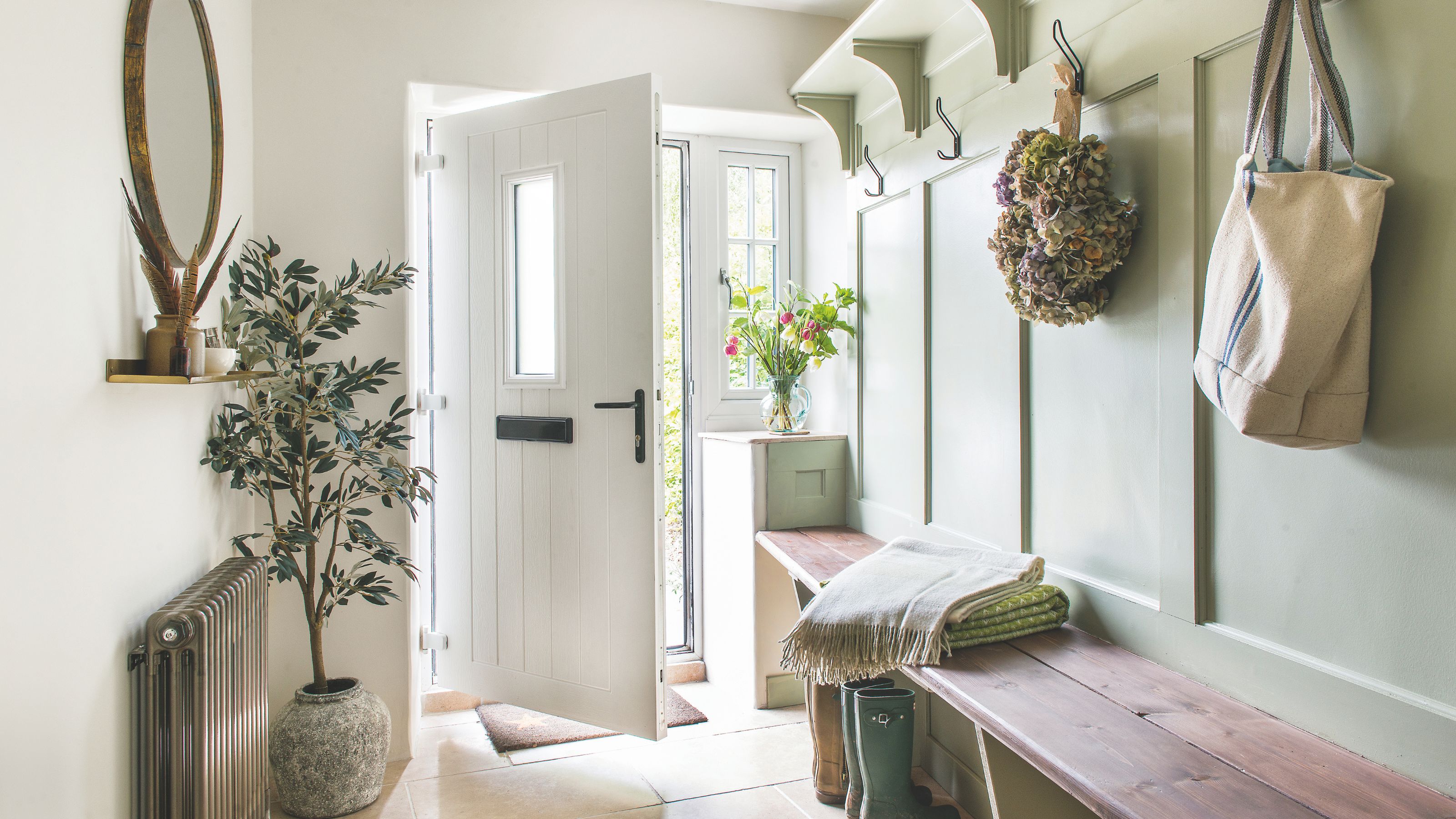 Country-style hallway with panelling on the walls and a wooden bench for seating. There's also a small tree beside the white front door