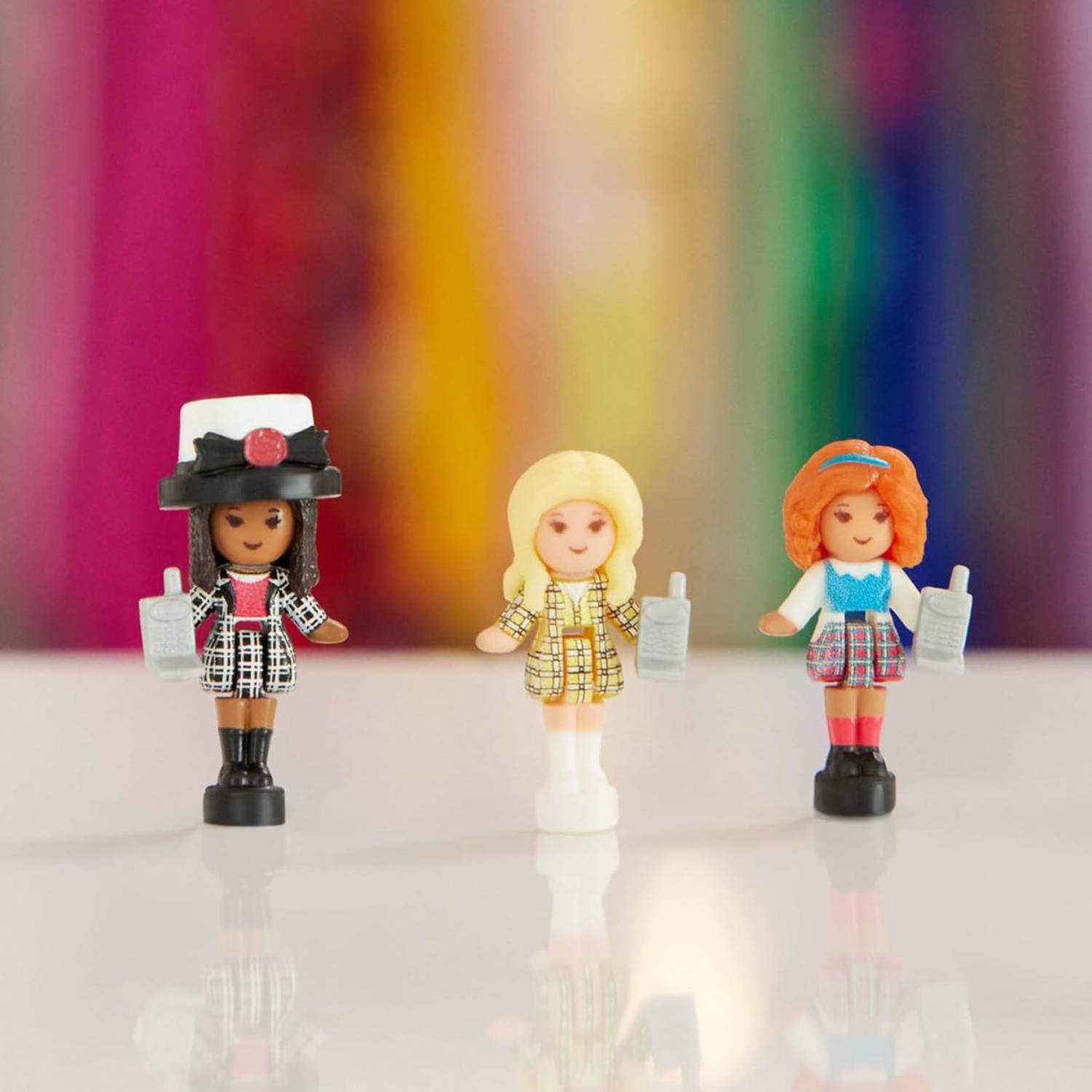 Image of the three Clueless-themed Pollys&#039; as found on the Clueless Polly Pocket set, sitting on a white table with a rainbow background.