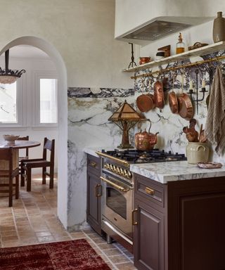 Brown kitchen cabinets framing a traditional range cooker surrounded by marble tiles