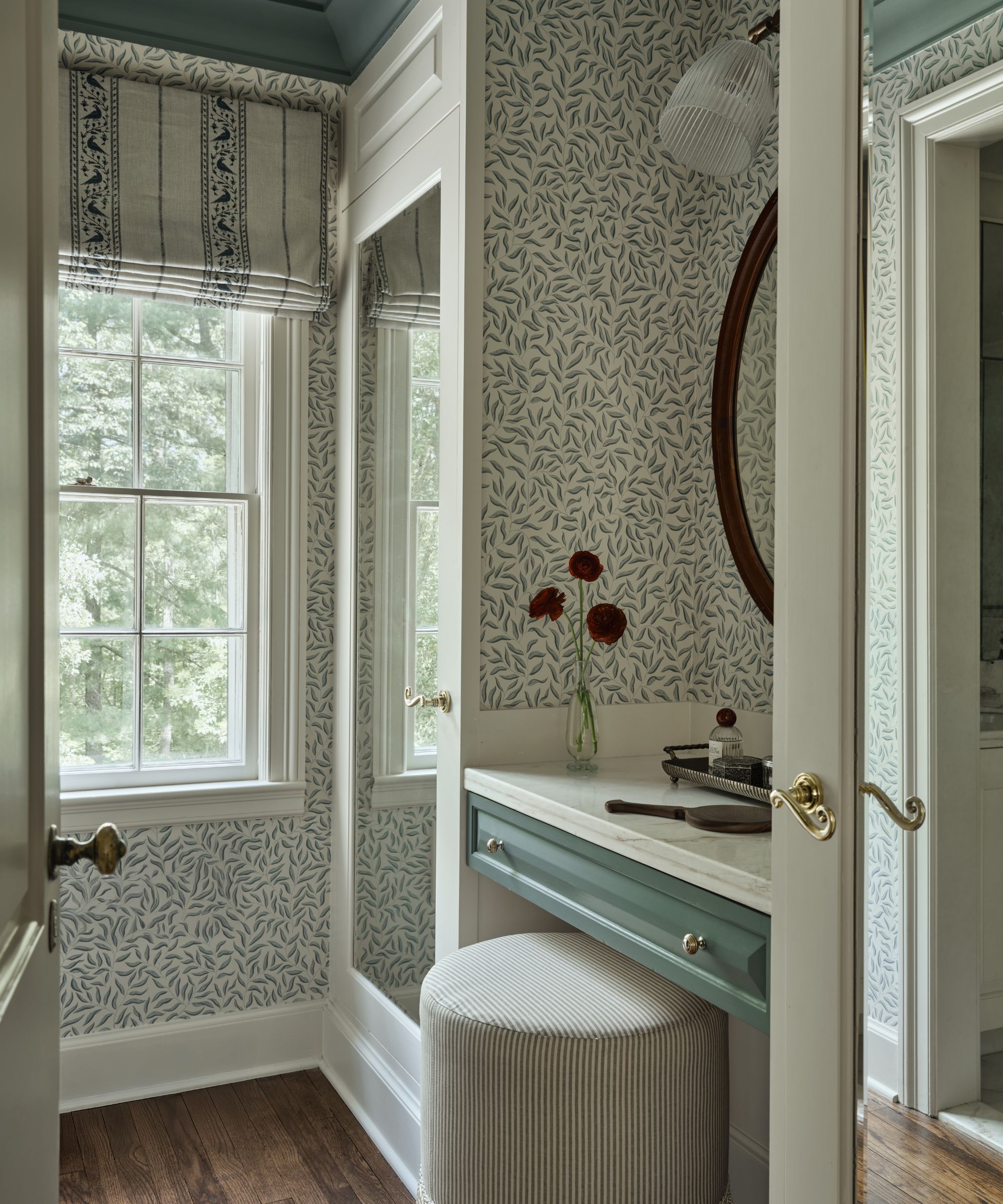a small dressing room with leafy green wallpaper, a painted green ceiling and small vanity table and striped stool