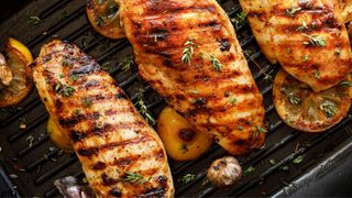 Three grilled chicken breasts with thyme and rosemary on cast iron tray