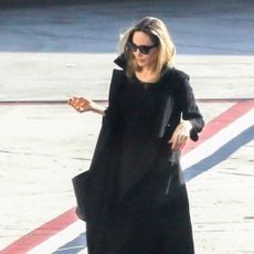 Angelina Jolie exits a plane wearing a black dress with a black coat and black bag plus sandals