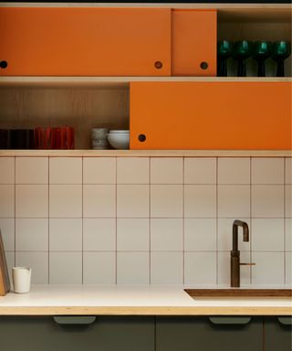 An orange and green kitchen with white tiles and orange grout