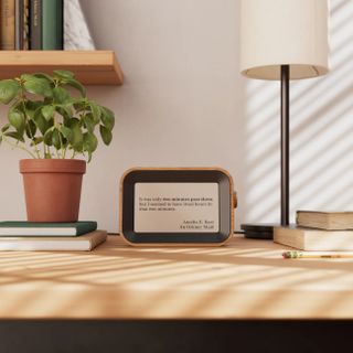 A small Author Clock on a wooden desk between a green plant and a small lamp