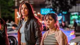 (L to R) Melissa Barrera as Sam Carpenter, Jenna Ortega as Tara Carpenter standing in the streets with cop cars behind them and red light hitting their hair in Scream VI