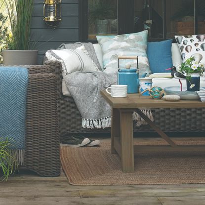 Rattan sofas and wooden coffee table on wooden decking with blue and white cushions