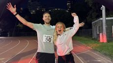 Man and woman standing on running track look at camera and cheer in celebration with arms outstretched