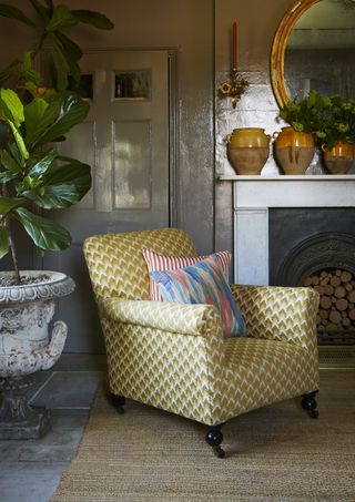 grey living room with slate floor, coir rug, yellow patterned armchair, spring coloured cushions/pillows, pots on mantel, flowers, wall light, mirror, urn with plant