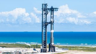 a huge silver rocket stands on a seaside launch pad