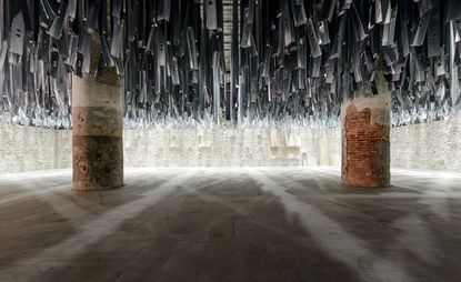 Large room with stone floor, two pillars and hundreds of metal shards pointing down from the ceiling