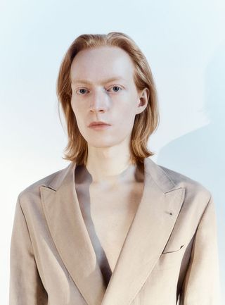 Model wears Brunello Cucinelli's men's suit jacket on a pale blue background