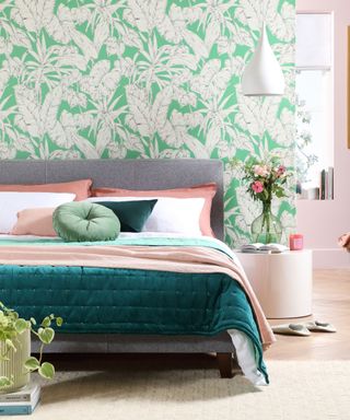 A bedroom with a green leafy wallpaper, a gray bed with pink and green bedding, and a pink wall in the distance