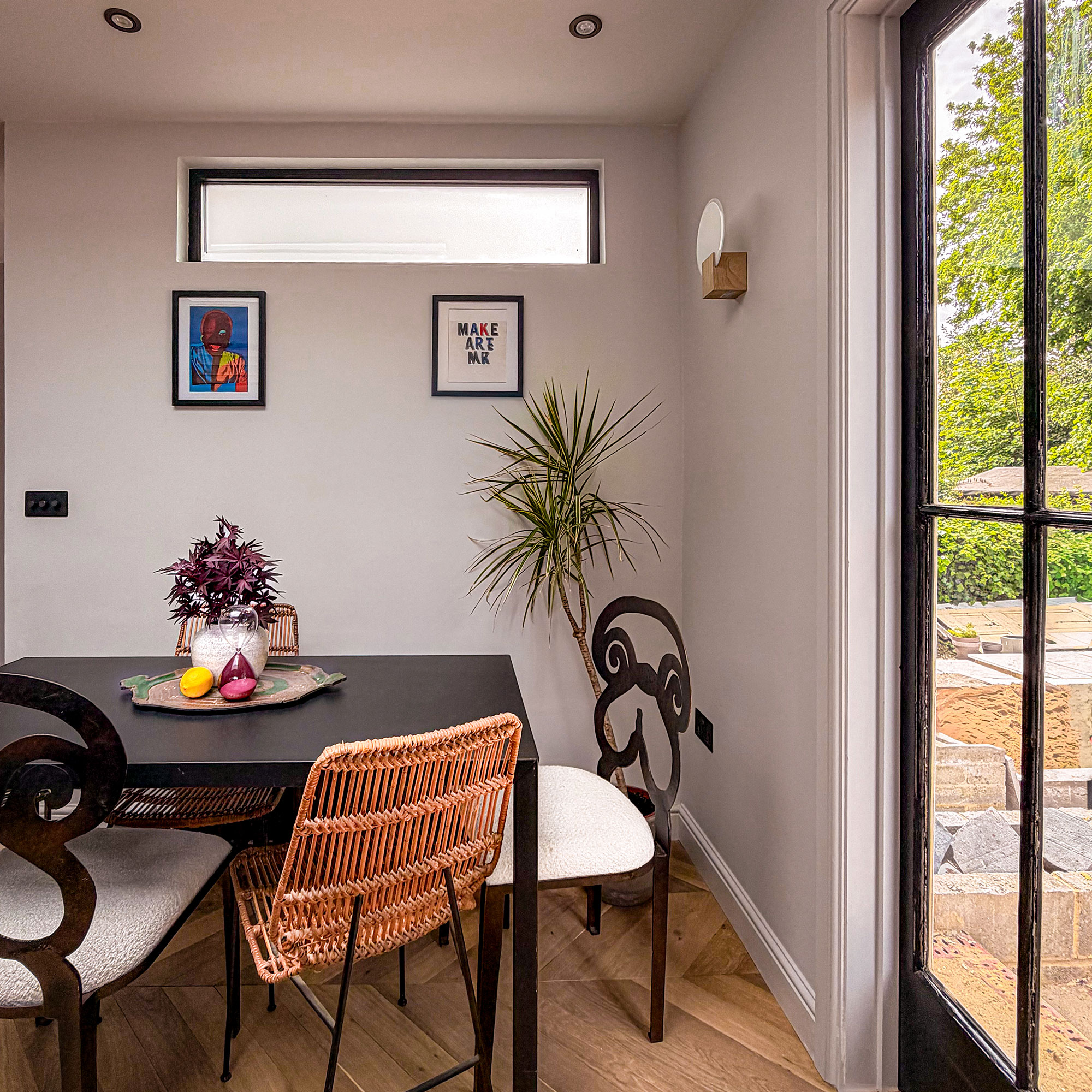 Dining area with black table and three chairs, with vase in centre, beside doors to garden